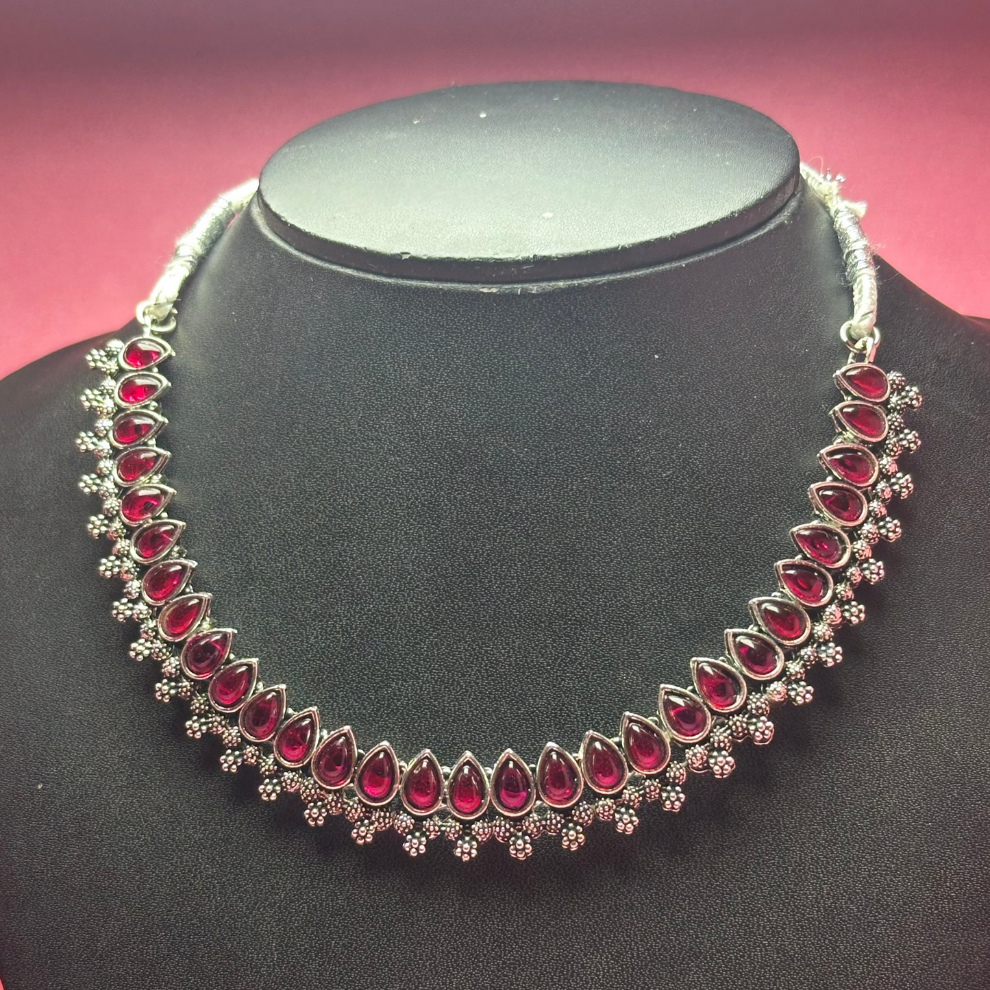 Necklace with red gemstones on a black mannequin against a pink background