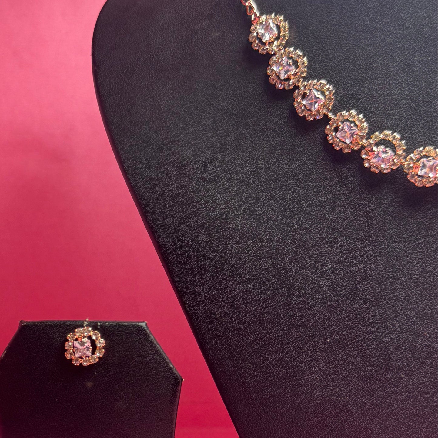 Necklace on a black stand against a pink background