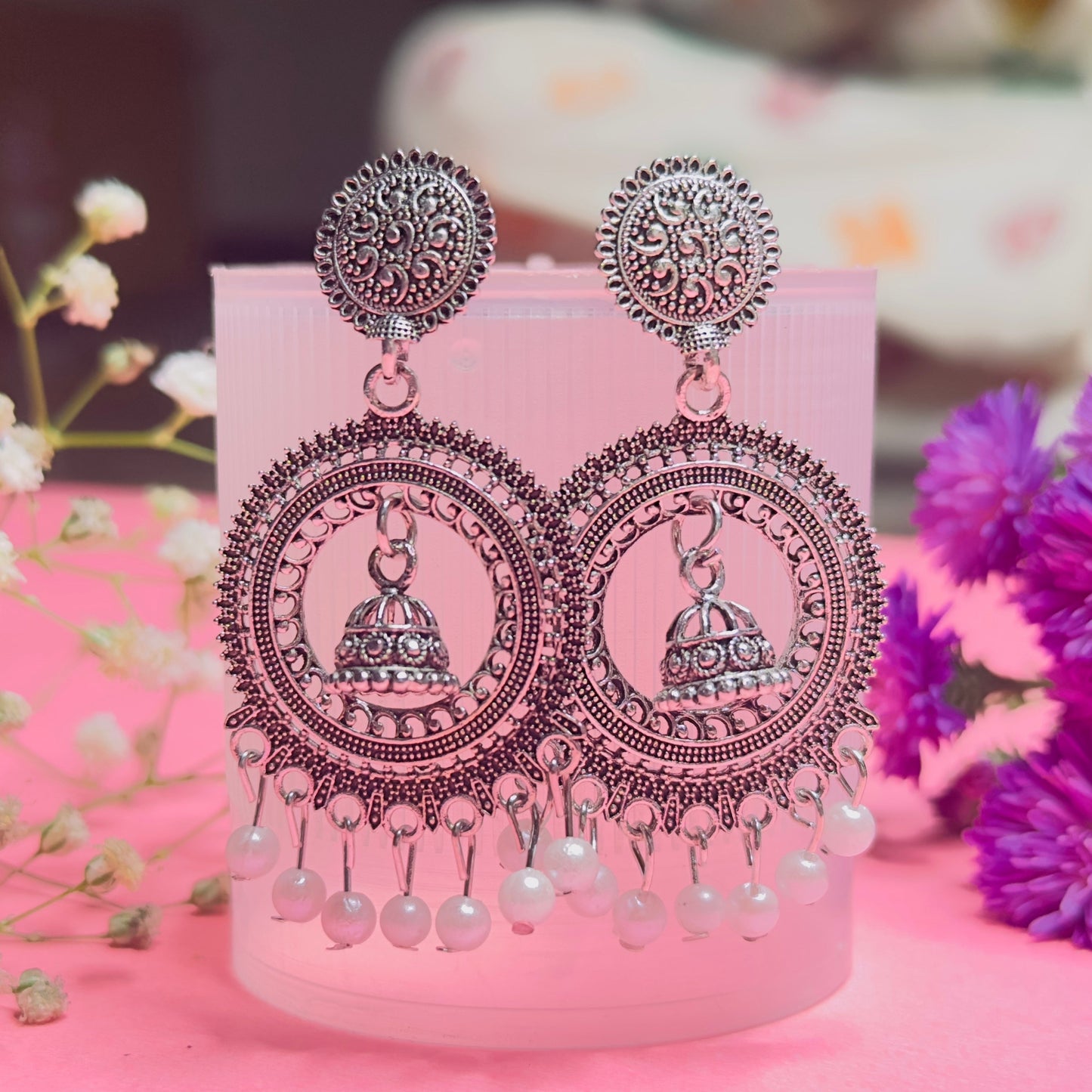 Decorative earrings on a pink stand with flowers in the background