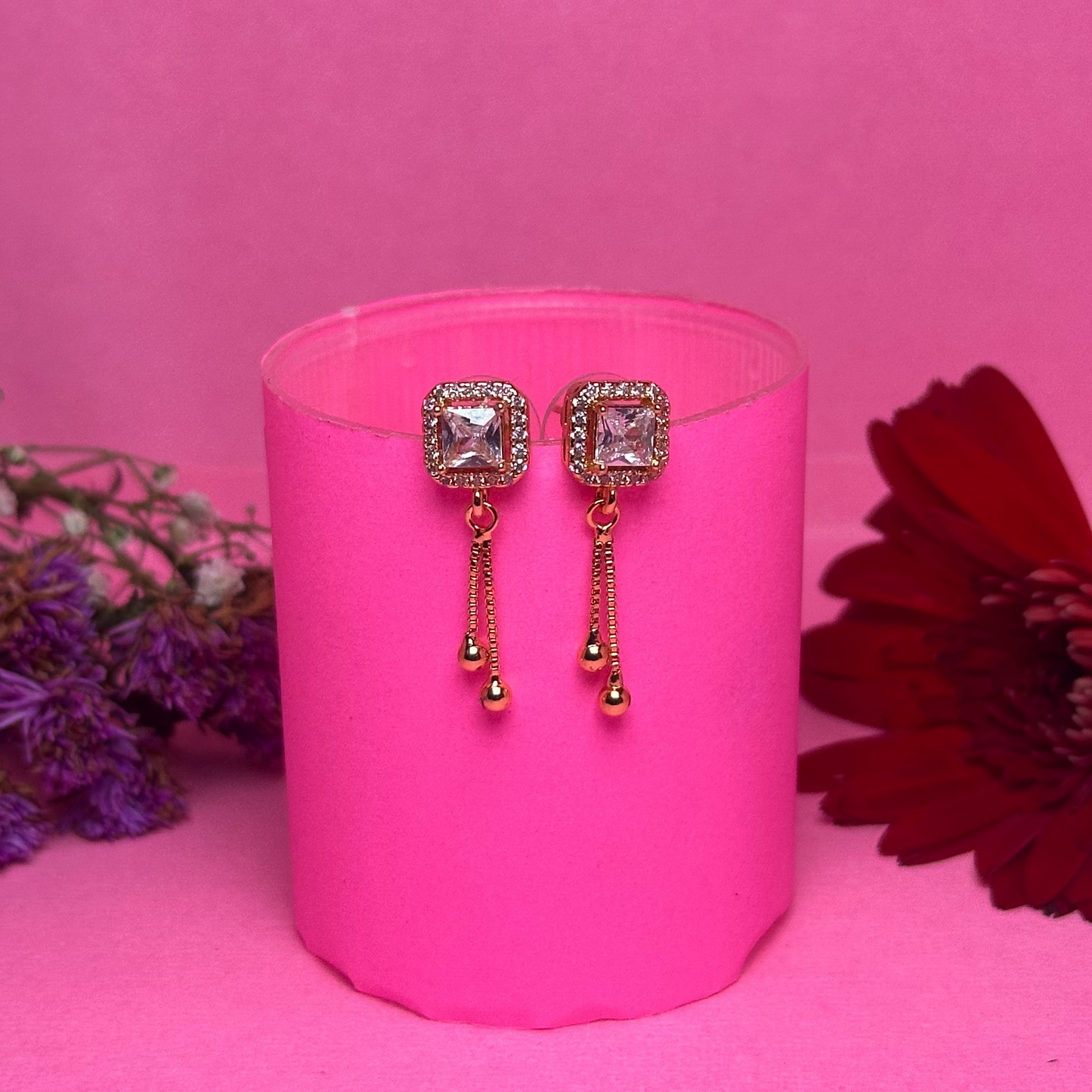 Pair of earrings on a pink stand with flowers on a pink background
