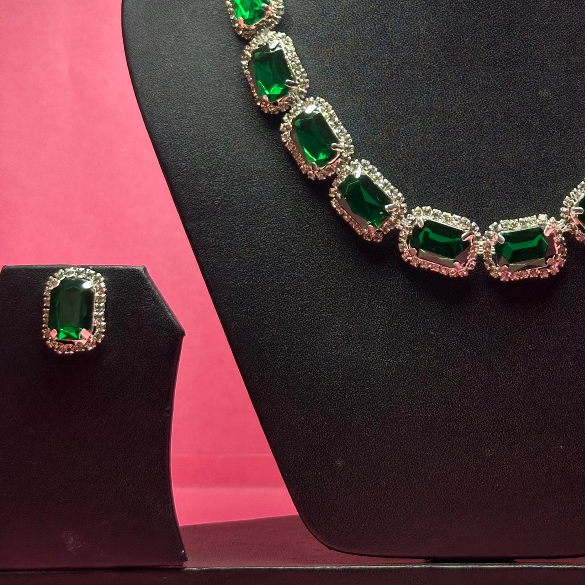 Green gemstone necklace and earrings on a black mannequin bust against a pink background