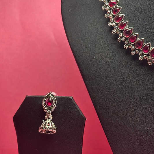 Jewelry set with necklace and earring on black stands against a pink background