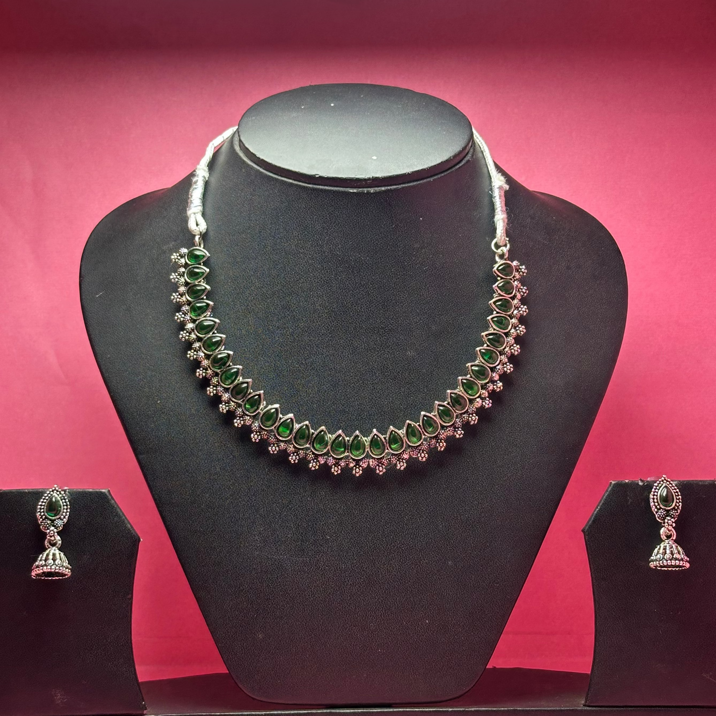 Necklace and earrings set on a black mannequin bust with a pink background
