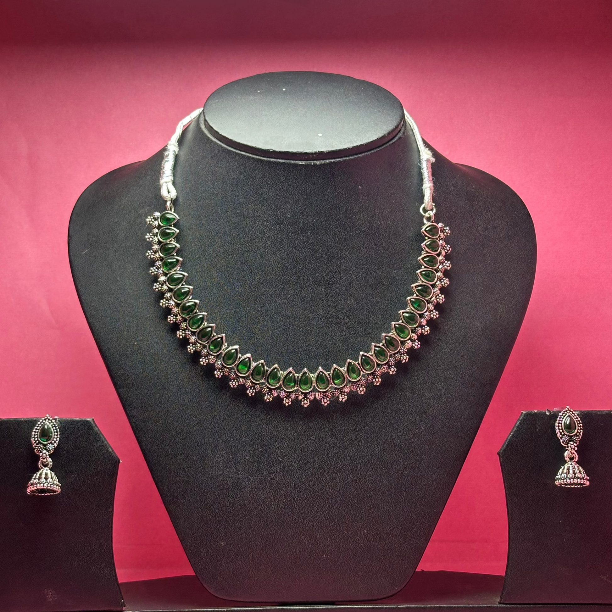 Necklace and earrings set on a black mannequin bust with a pink background