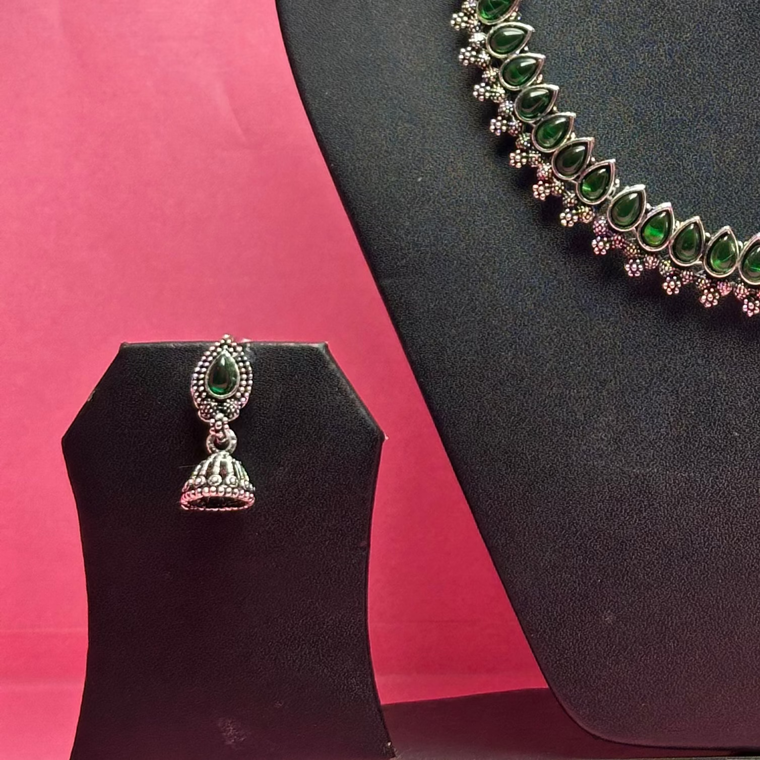 Jewelry set with necklace and earrings on a black mannequin bust against a pink background