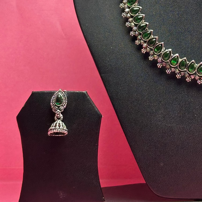 Jewelry set with necklace and earrings on a black mannequin bust against a pink background