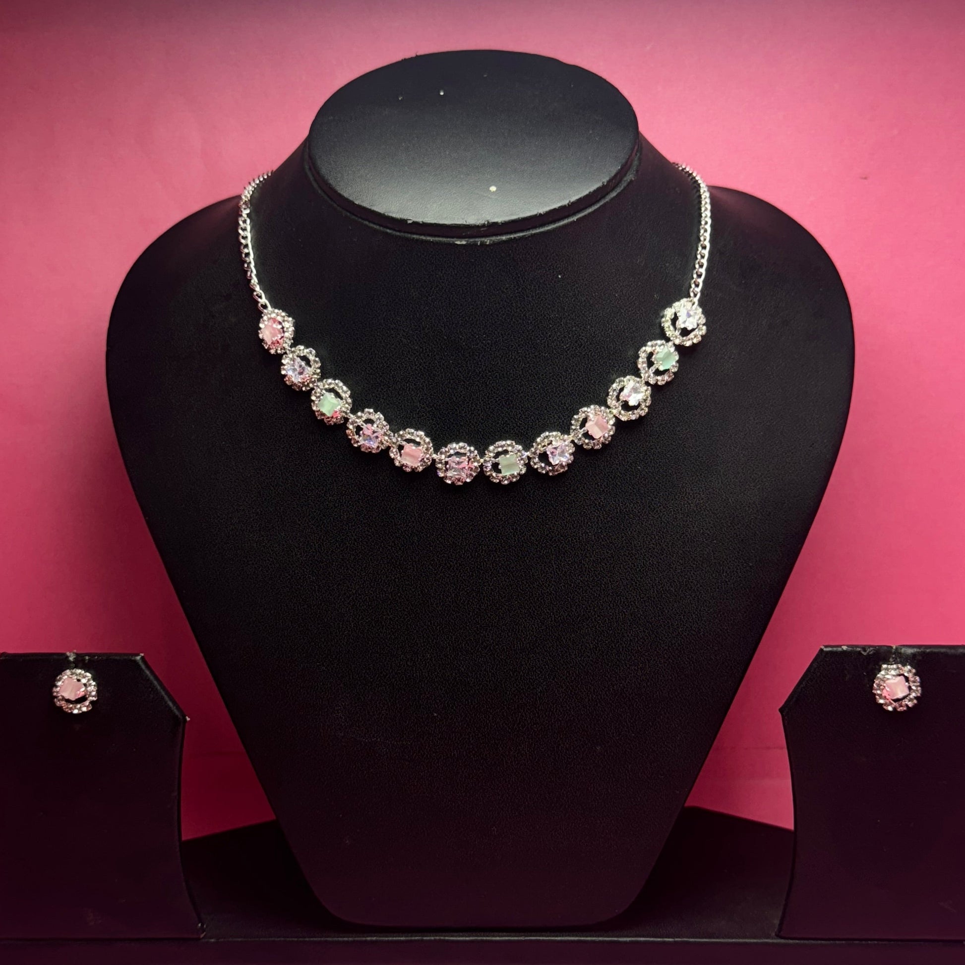 Black jewelry display with a bracelet and earrings against a pink wall