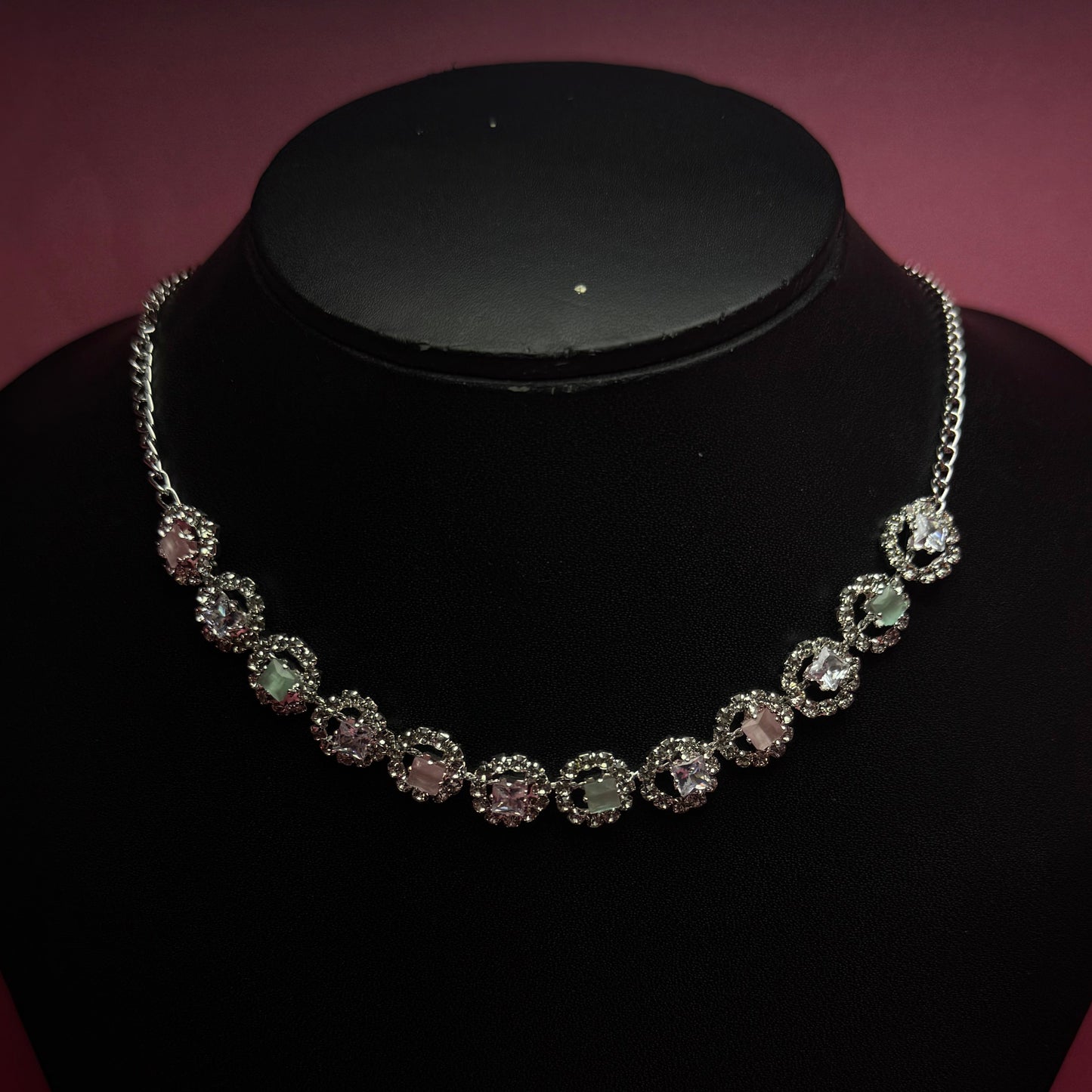 Silver necklace with clear stones on a black stand against a dark background