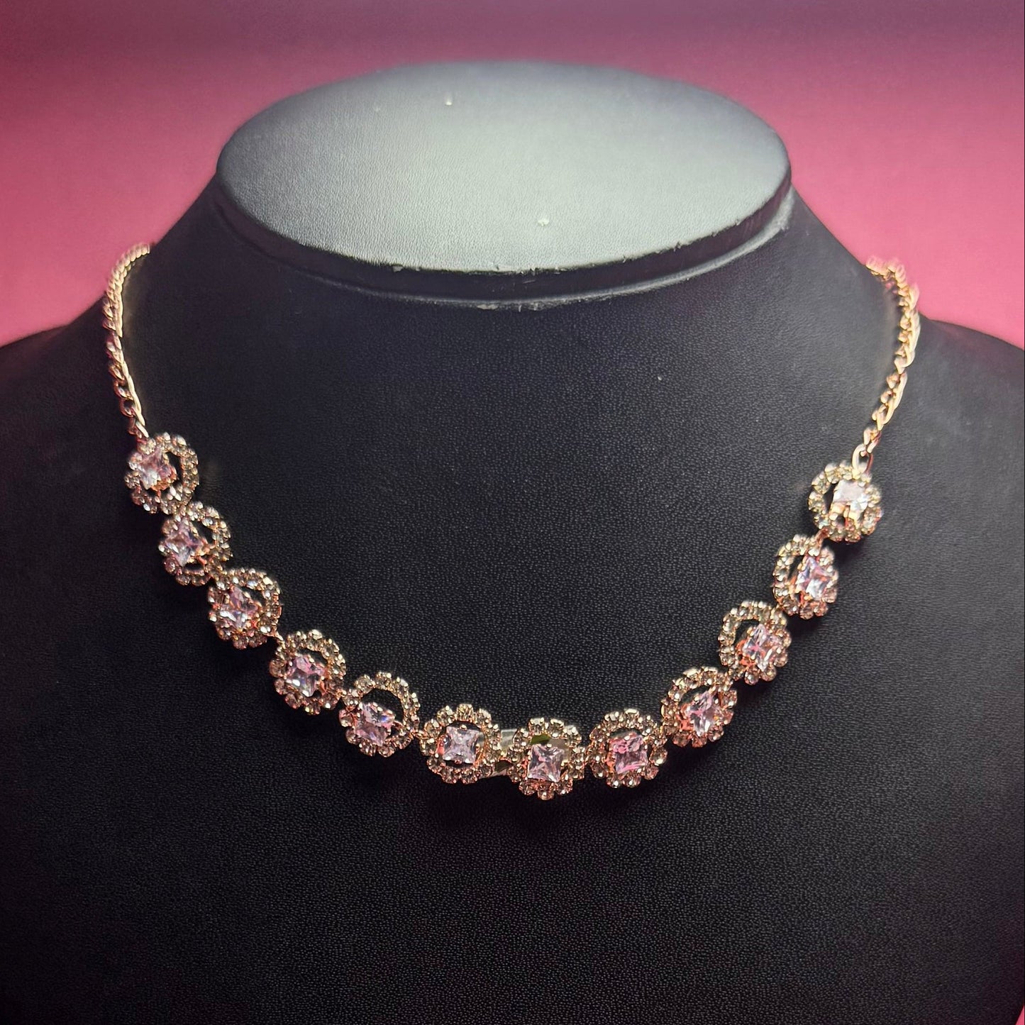 Necklace and earrings set on a black mannequin bust with a pink background