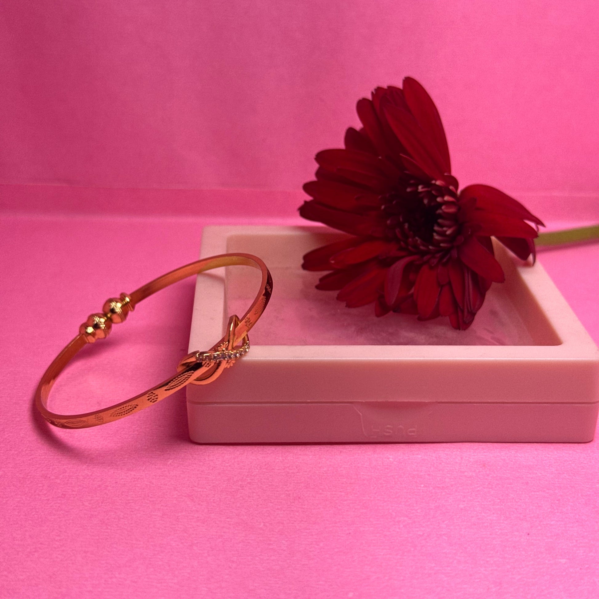 Gold bracelet with a red flower on a pink background