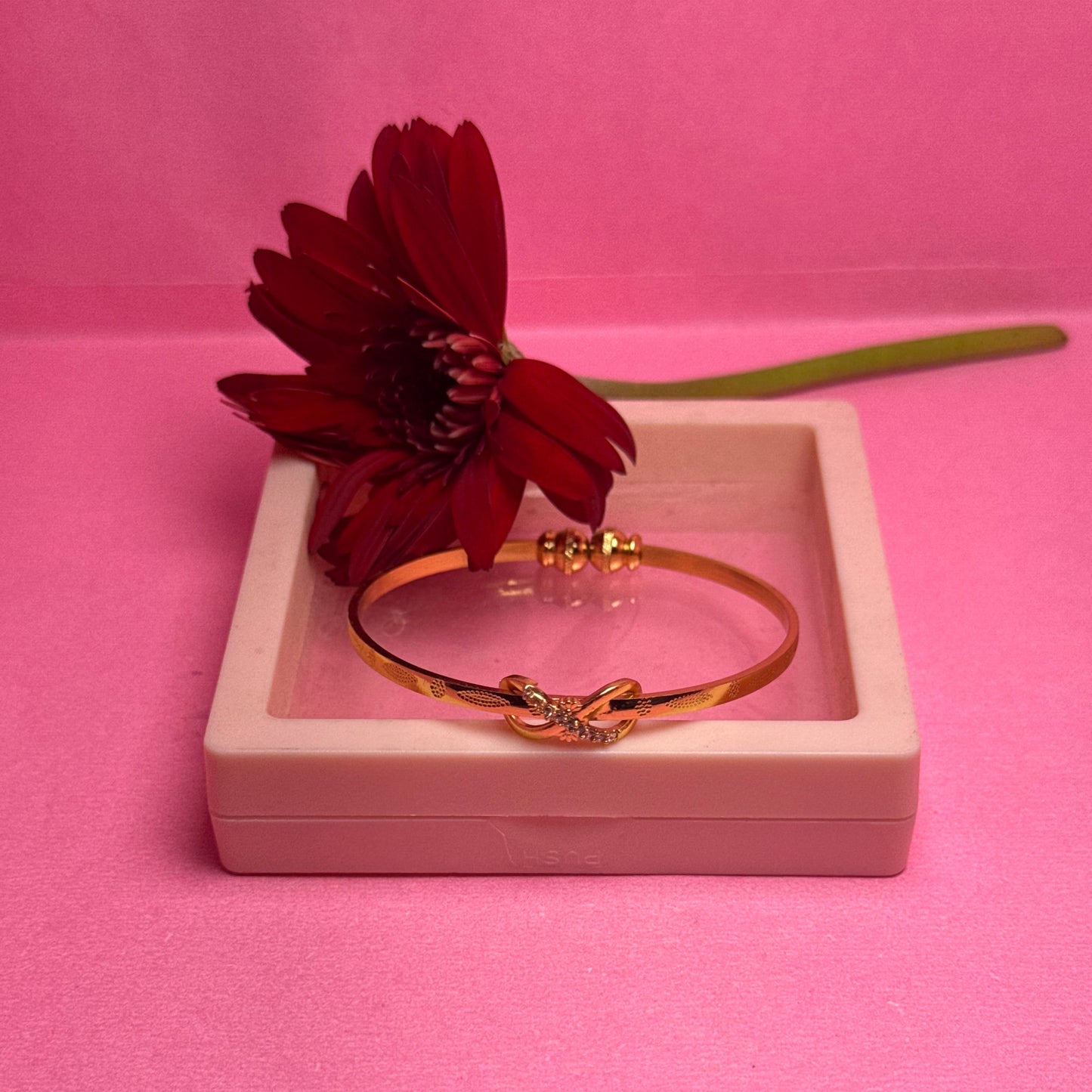 Gold bracelet and red flower in a white box on a pink background