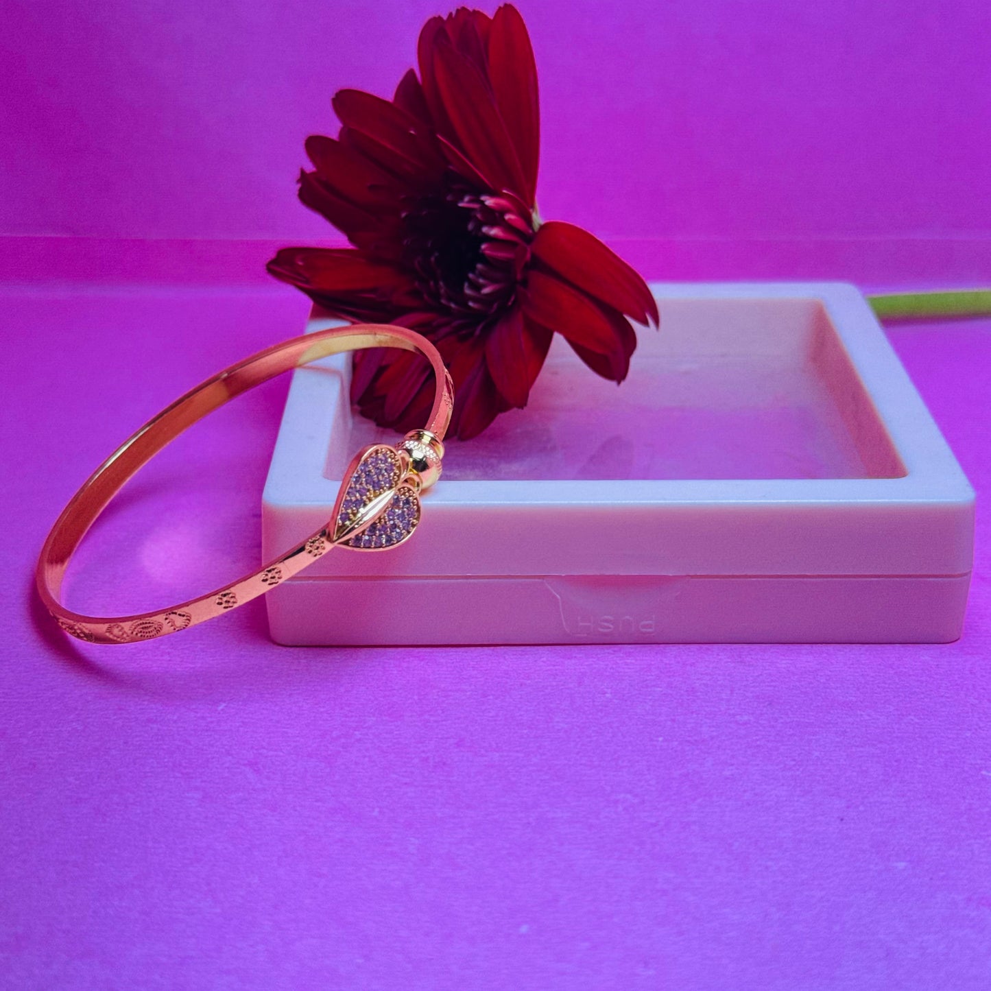 Rose gold bracelet with heart details on a pink surface with a red flower.